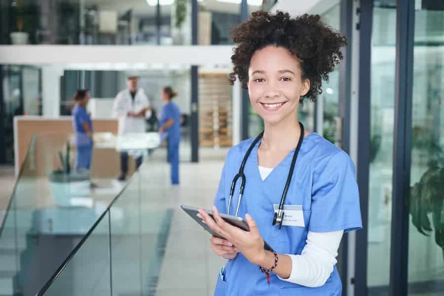 young medical assistant in scrubs holding tablet and smiling