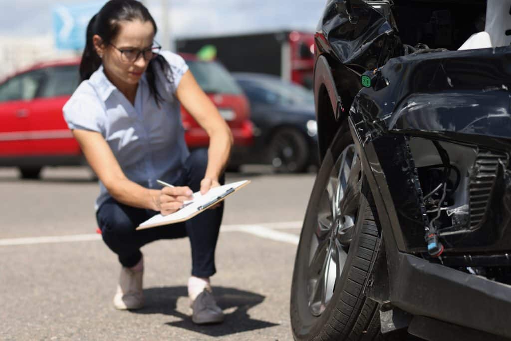 Woman inspecting damaged car and writing on clipboard