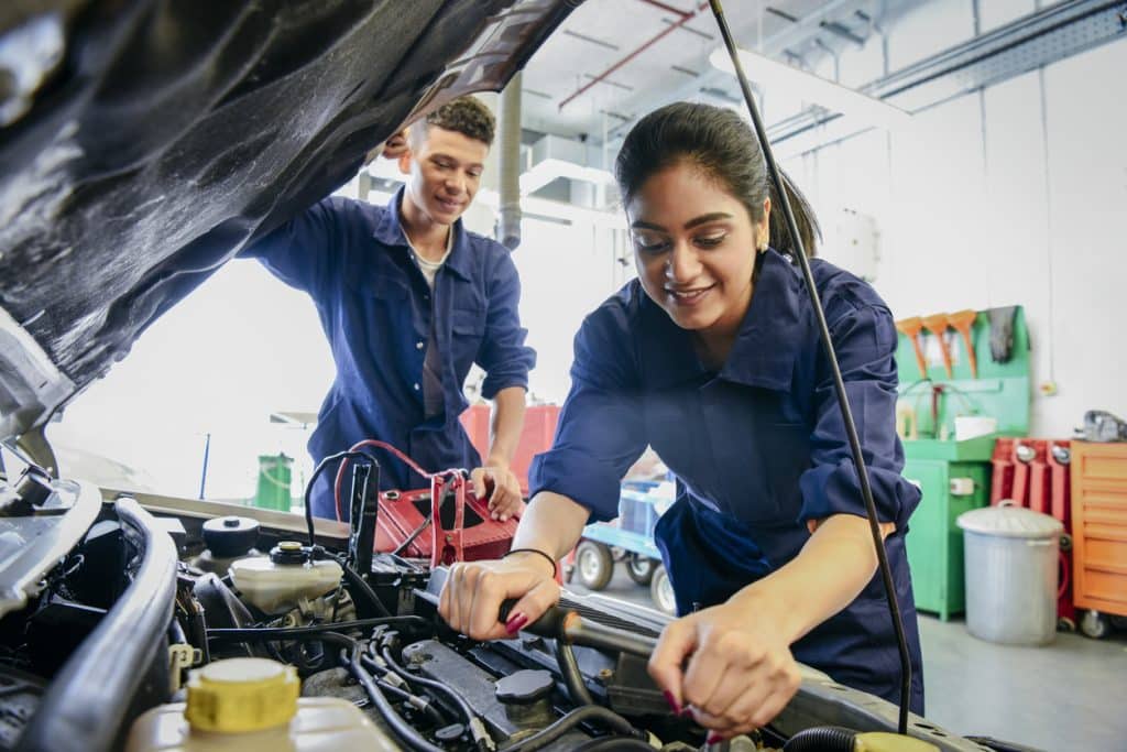 Student mechanics work under the hood of car at vocational school