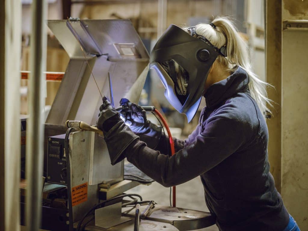 Welder wearing protective face mask repairs equipment in production facility