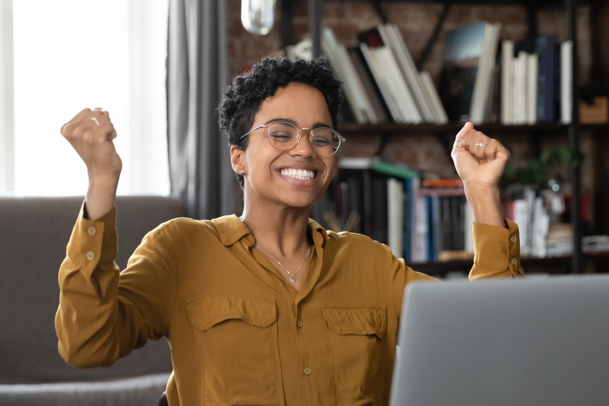 New student smiles and lifts arms in celebration while looking at open laptop computer