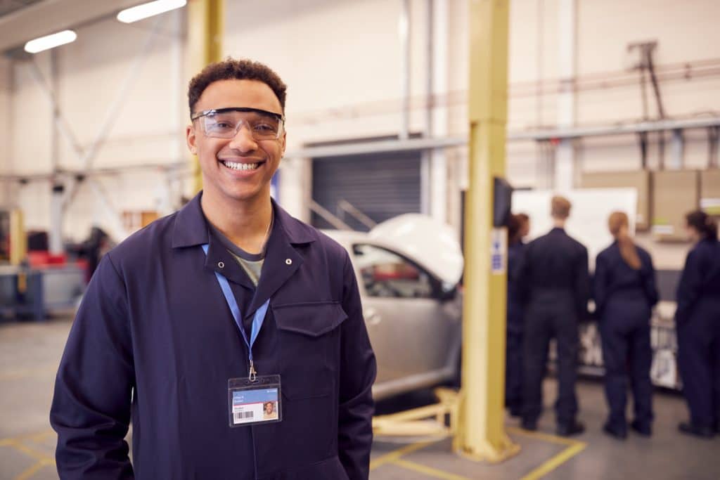 Graduate of automotive program poses with protective gear in auto repair shop