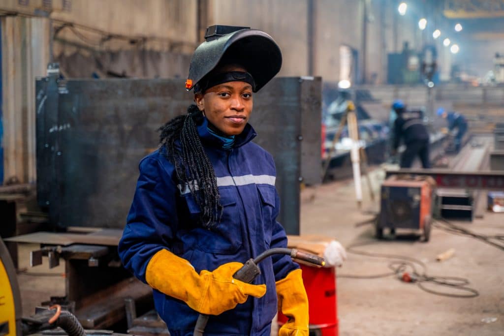Graduate of welding program poses with protective gear in large shop