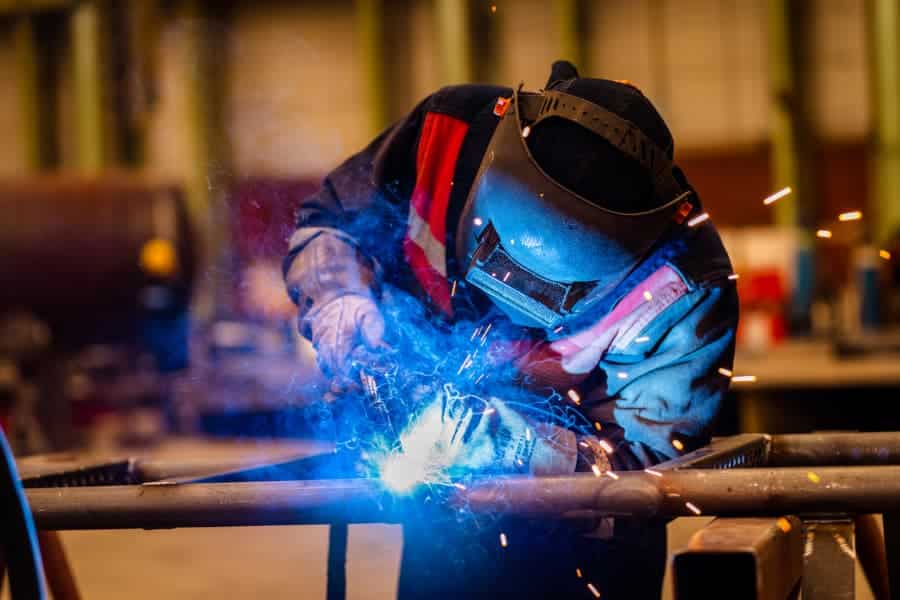 Student wearing protective equipment while welding steel pipes together