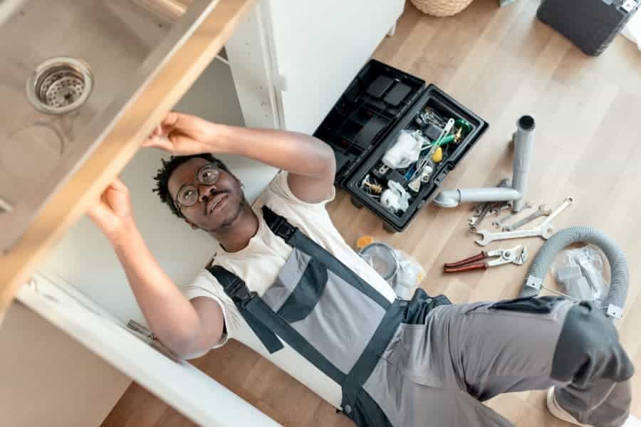 Plumber working under sink with toolbox nearby
